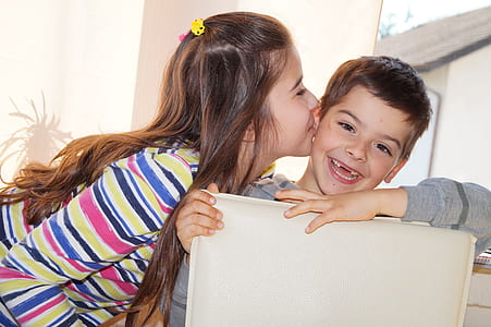 girl kisses smiling boy while sitting on gray leather dining chair during daytime thumbnail