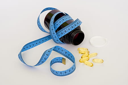 Blue Tape Measure Wrapping Black Medication Pill Bottle With White Cap thumbnail