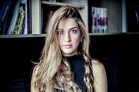 woman with blonds hair sitting beside wooden bookcase inside well lighted room thumbnail