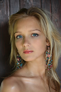 woman wearing jeweled and gold hook earrings standing in front of brown wall thumbnail