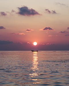 black boat surrounded by blue ocean during orange sunset thumbnail
