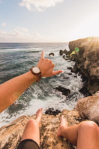 man sitting on rock beside ocean doing devil's horn hand gesture thumbnail