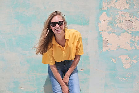 Young Woman Wearing Yellow Polo Shirt And Sunglasses Standing in Front of Teal Concrete Wall thumbnail