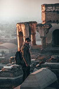 Man Wearing Cap and Backpack Standing on Ruins thumbnail