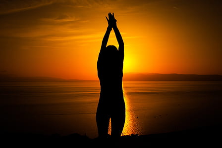 silhouette of woman standing on hill near body of water during sunset thumbnail
