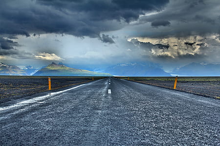 straight asphalt road near mountain under grey clouds blue skies thumbnail