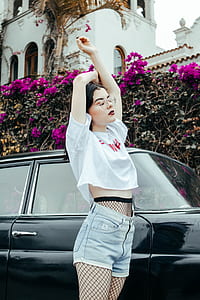 woman in white top and gray denim shorts raising her hands near black car thumbnail