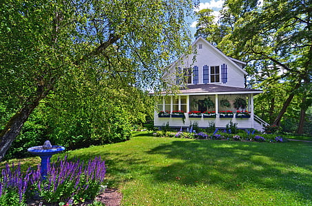 white and brown wooden house on green field with trees and purple flowers landscape photography thumbnail