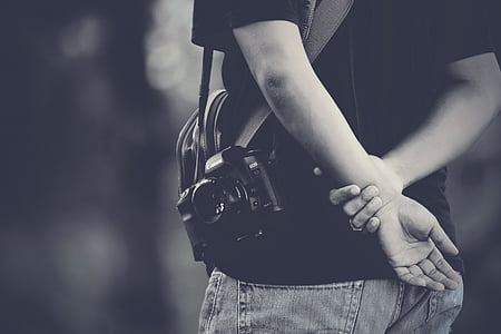 DSLR camera hanging on person's left shoulder in grayscale photography thumbnail