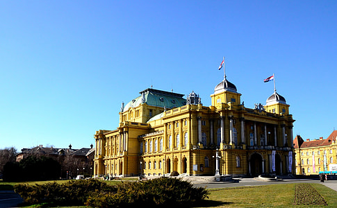 yellow concrete building with two flags under blue sky during daytime thumbnail