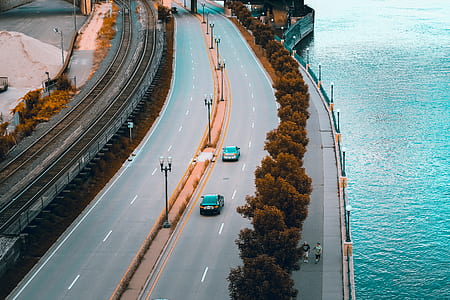 two black vehicles travelling on road near body of water thumbnail